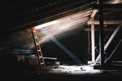 A wooden ladder leading up to an illuminated space in a dark attic.
