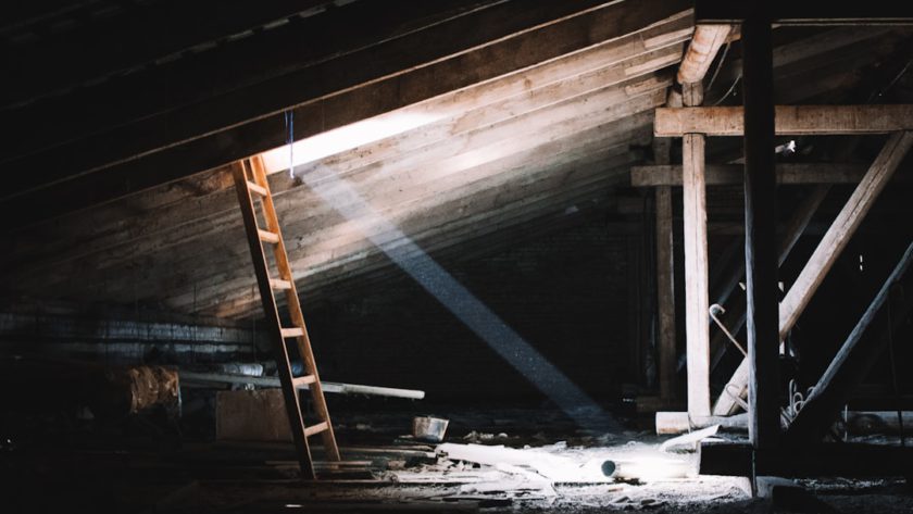 A wooden ladder leading up to an illuminated space in a dark attic.